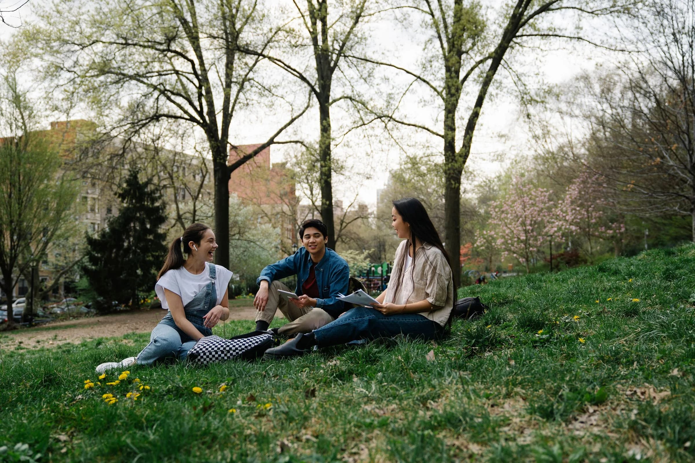 Three students sitting together with notebooks in a city park.